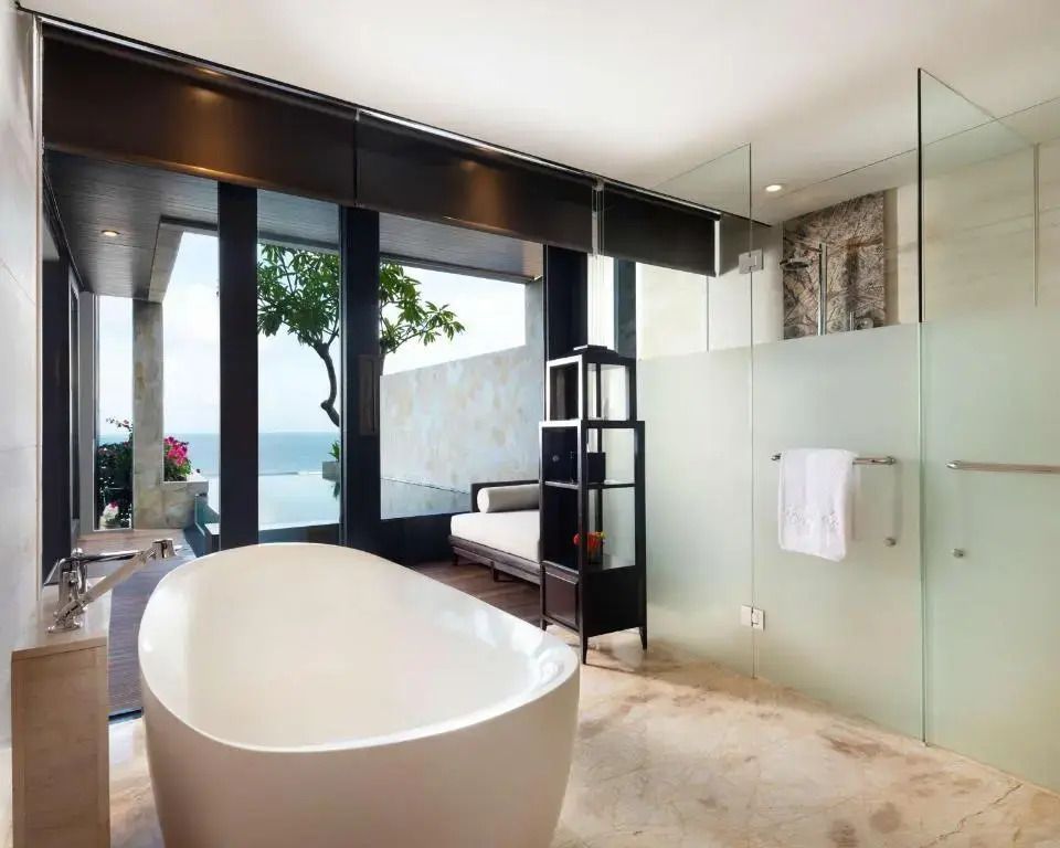 Badezimmer mit freistehender Badewanne und Meerblick durch große Fenster.