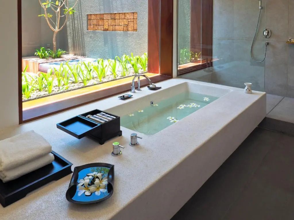 Badezimmer mit eingelassener Badewanne und Blick in den grünen Innenhof.