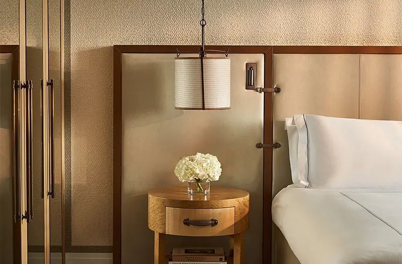Nachttisch mit Blumen und Lampe an einer gepolsterten Wand in Deluxe Doppel Junior-Suite.