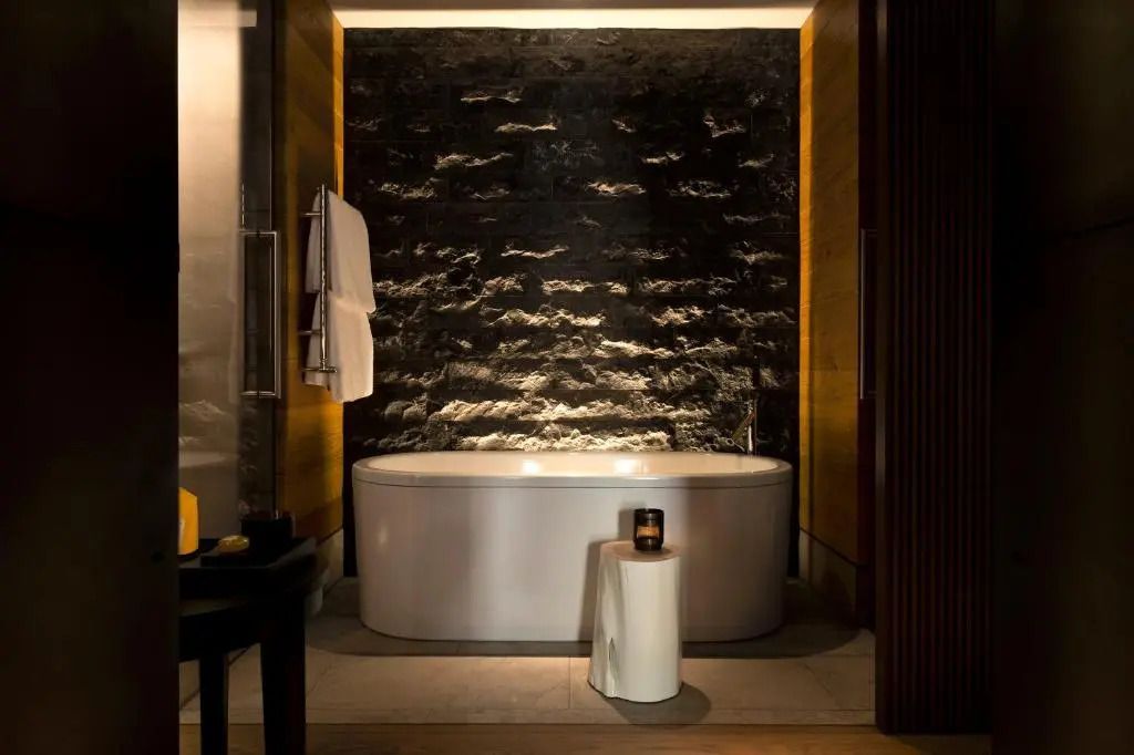 Design-Badezimmer mit beleuchteter Steinwand und freistehender Badewanne