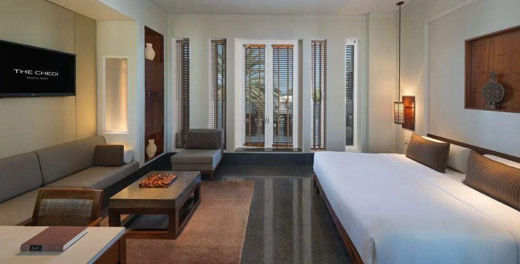 Elegantes Zimmer mit großem Bett, Sitzbereich und Fenstern mit Lamellenläden.