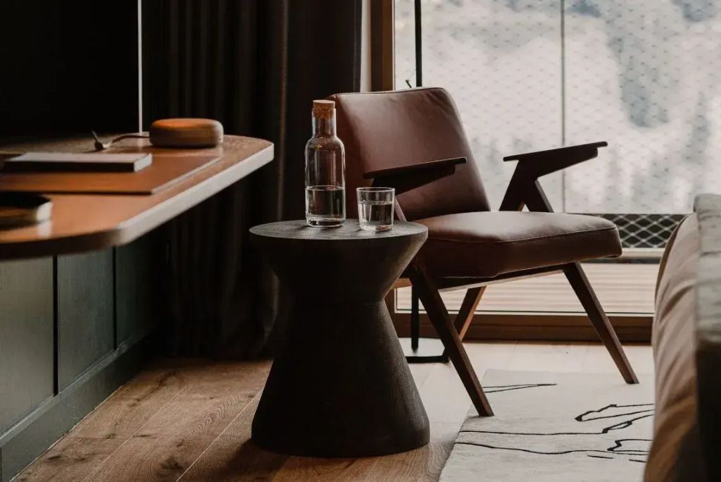 Eleganter Tisch mit Wasserflasche und Glas neben einem Designerstuhl