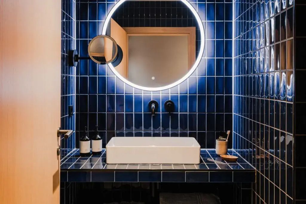 Blau gefliestes Badezimmer mit rundem Spiegel und eleganter Beleuchtung