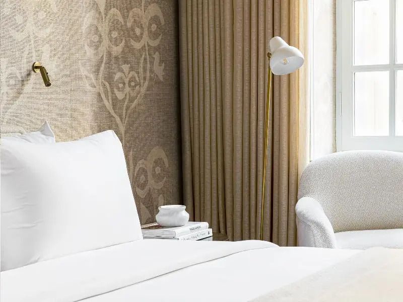 Seitenansicht des Hotelbettes mit beigem Vorhang und Leseleuchte