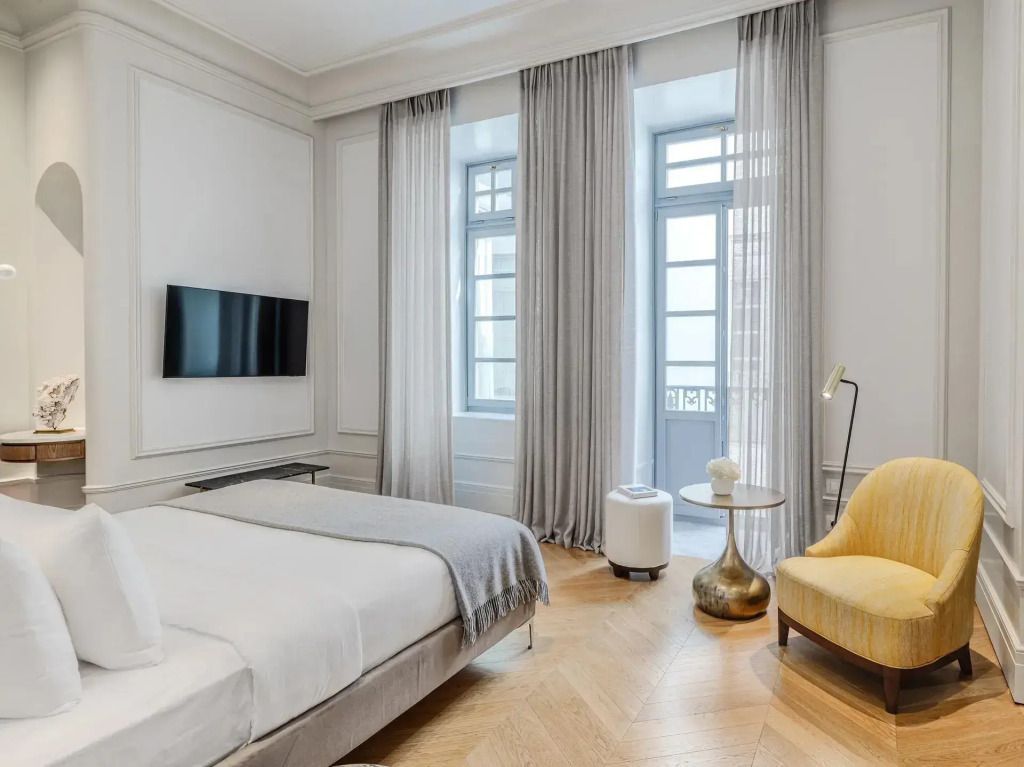 Elegantes Schlafzimmer mit Doppelbett, hellem Holzboden und großen Fenstern mit Vorhängen