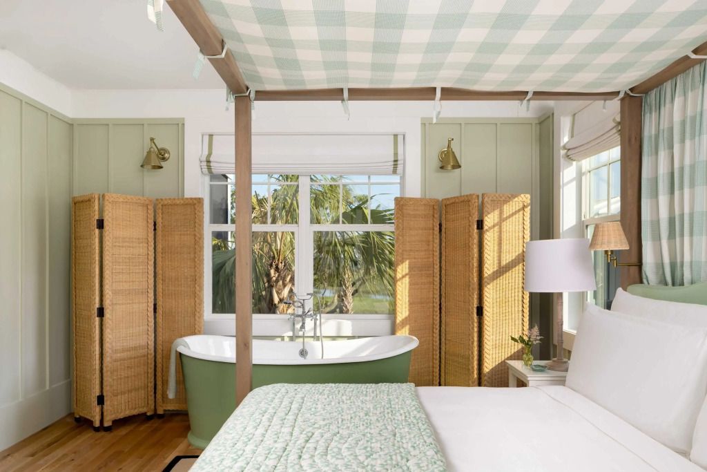 Helles Schlafzimmer mit Himmelbett und freistehender Badewanne vor einem Fenster
