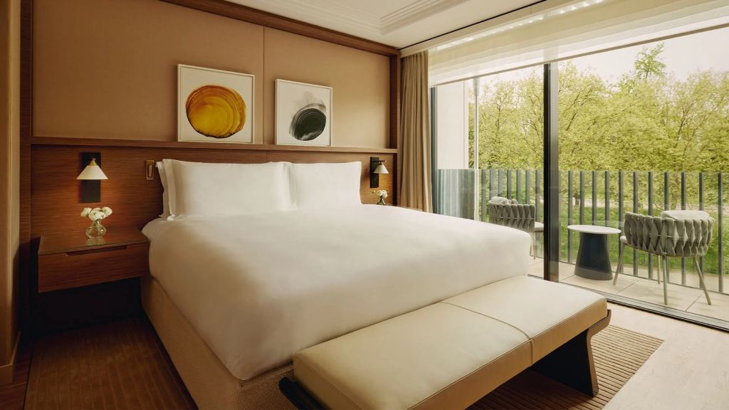Helles Zimmer mit großem Doppelbett und Zugang zu einem Balkon mit Blick ins Grüne.