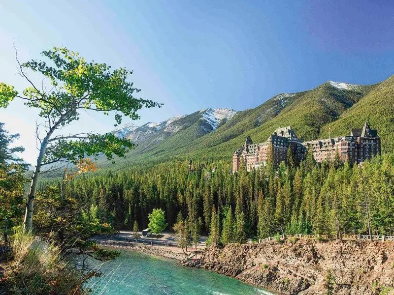 Hotel Fairmont Banff Springs eingebettet in grüne Berglandschaft mit Fluss im Vordergrund