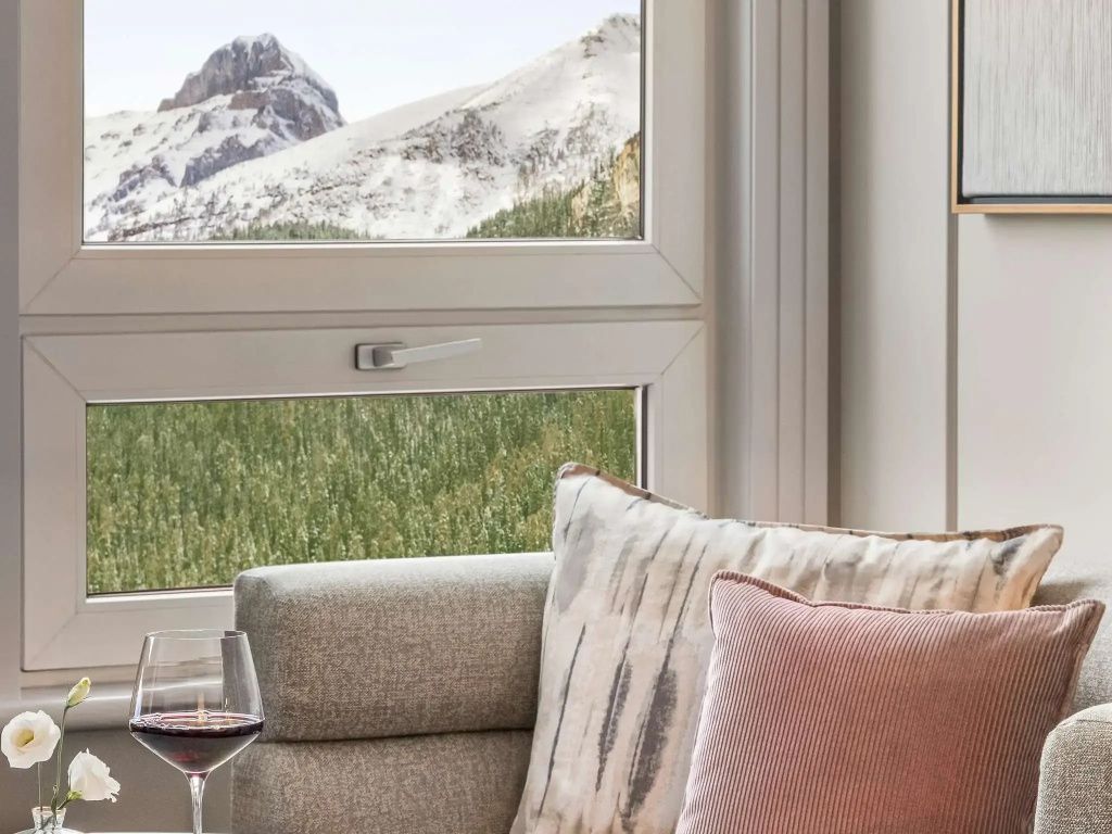 Fenster mit Blick auf schneebedeckte Berggipfel und Weinglas auf Sofa