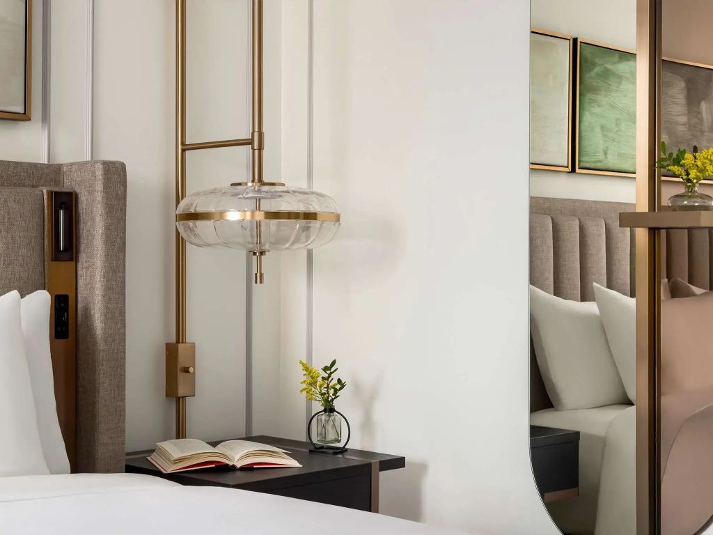 Nachttisch mit Buch und Blumenvase neben luxuriösem Bett