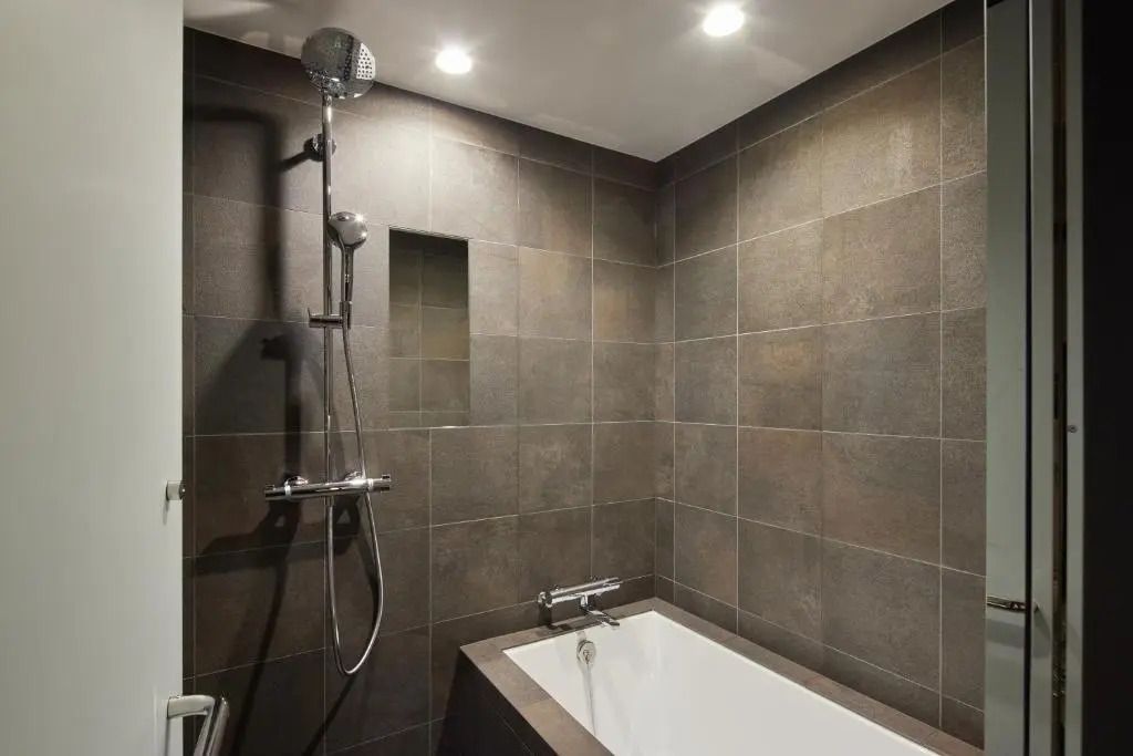 Modernes Badezimmer mit dunklen Fliesen und kombinierter Badewanne und Dusche