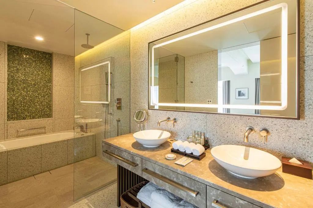 Luxuriöses Badezimmer mit Doppelwaschbecken, Spiegel mit Beleuchtung und ebenerdiger Dusche.
