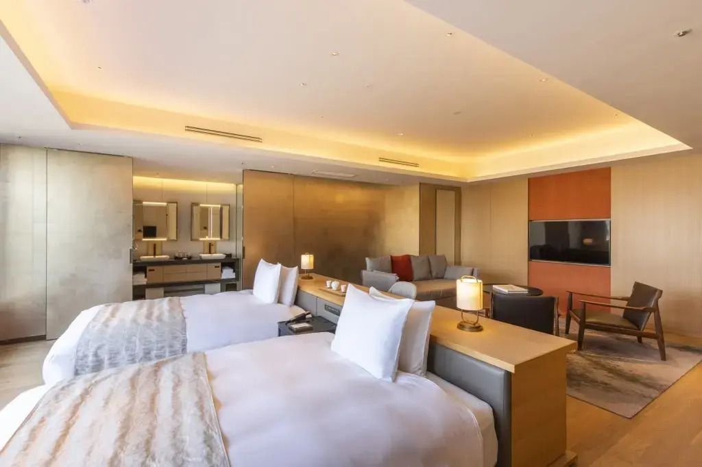 Moderne Junior-Suite mit zwei Betten, eleganter Beleuchtung und großem Spiegel.