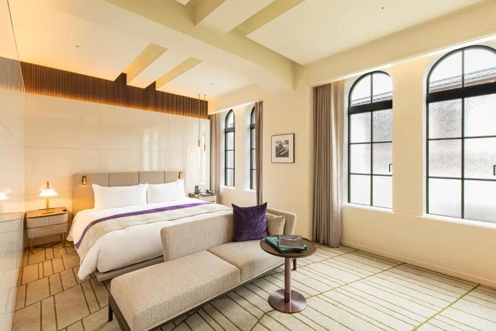 Elegantes Schlafzimmer mit Doppelbett, Sofa und großen Fenstern.