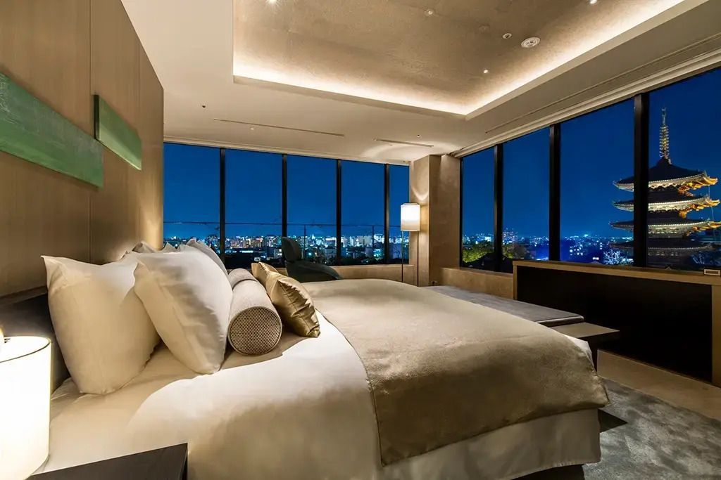 Sicht auf das elegante Schlafzimmer der Suite mit Panoramafenster und nächtlicher Stadtblick