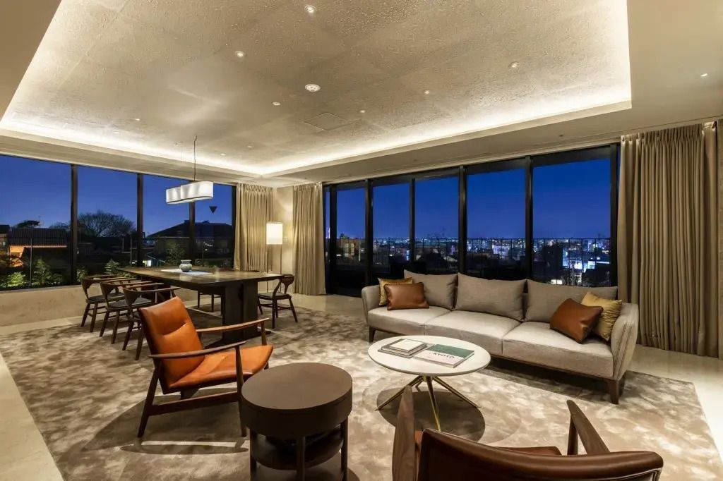 Wohnbereich der Suite mit modernen Möbeln und Panoramablick auf die Stadt bei Nacht