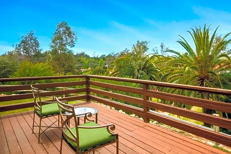 Holzbalkon mit Sitzgelegenheiten und idyllischem Blick auf Palmen und Gartenlandschaft.