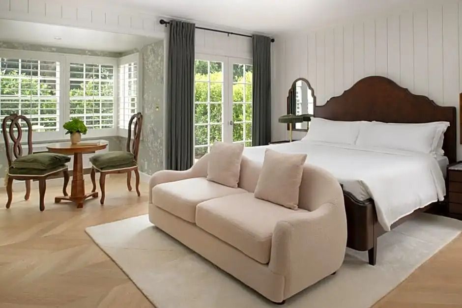 Helles Deluxe Zimmer mit eleganter Couch und großen Fenstern mit Gartenblick.