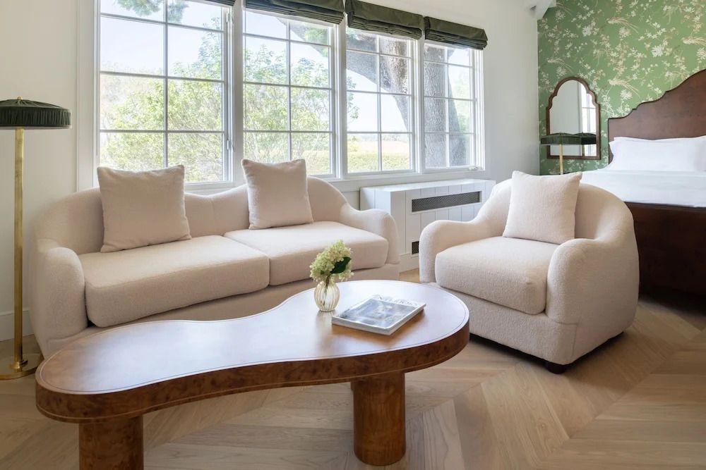 Helles Wohnzimmer mit großen Fenstern, beigen Sofas und stilvollem Holztisch.
