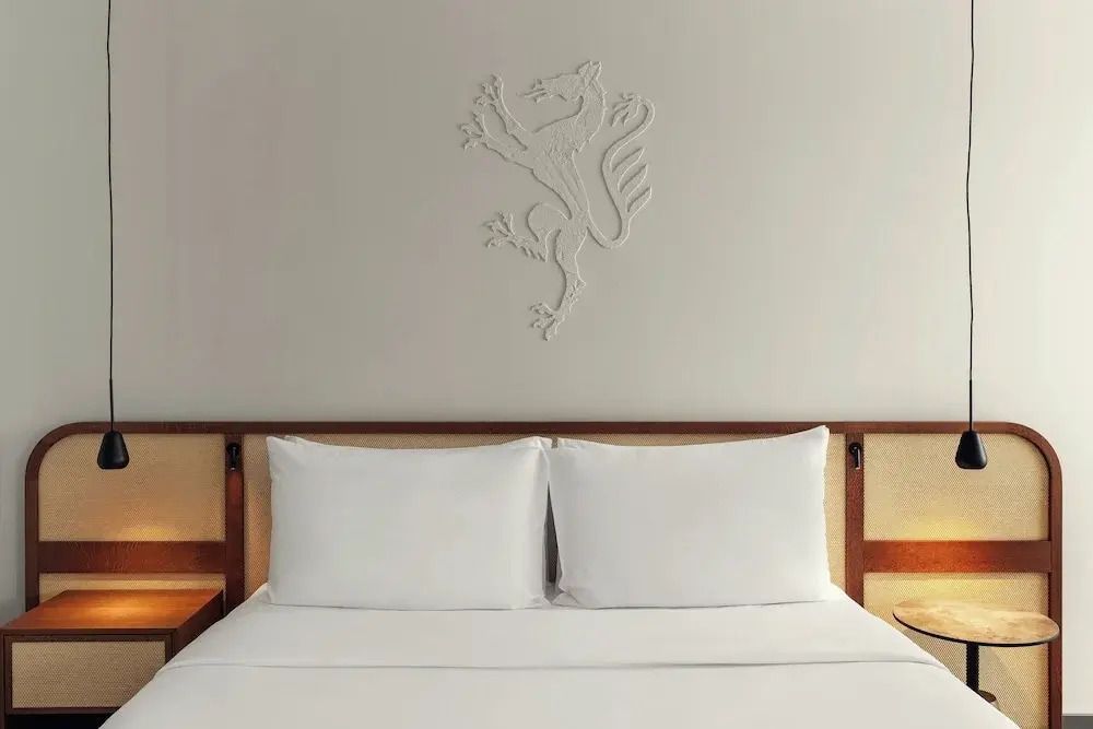 Doppelbett mit weißer Bettwäsche und dezentem Wandrelief eines Löwen