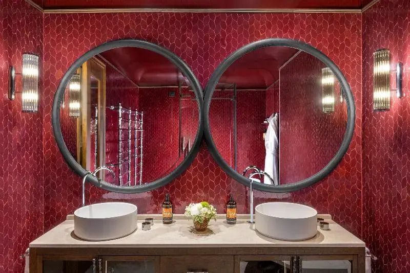 Luxuriöses Badezimmer mit zwei runden Spiegeln und stilvoller roter Fliesenwand.