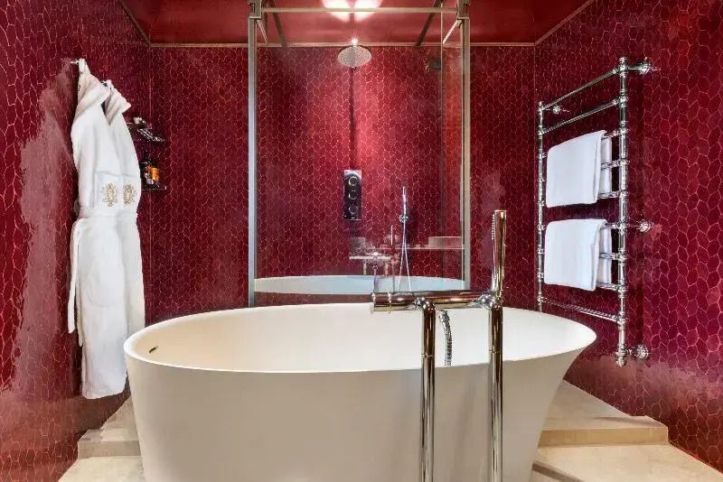 Moderne freistehende Badewanne vor edlen roten Wandfliesen mit gläserner Duschabtrennung.