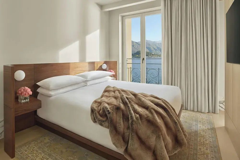 Doppelbett mit weicher Decke und Blick auf den See durch bodentiefe Fenster