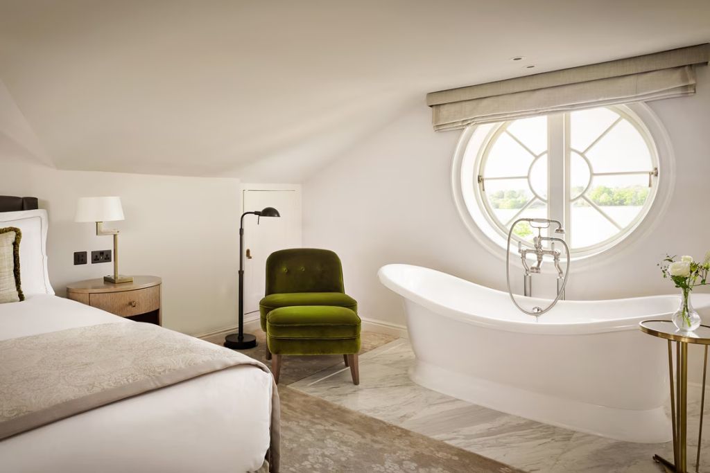Gemütliches Zimmer mit freistehender Badewanne. Großes, rundes Fenster mit Blick auf Grün.