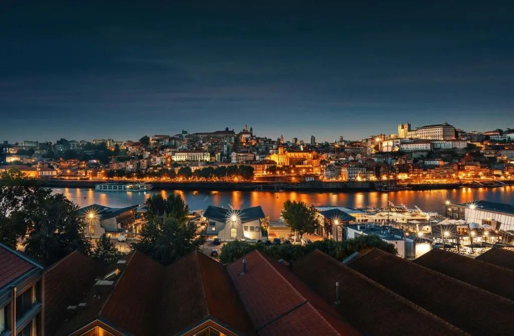 Abendliche Panoramaaufnahme der Stadtlandschaft mit beleuchteten Gebäuden am Flussufer.