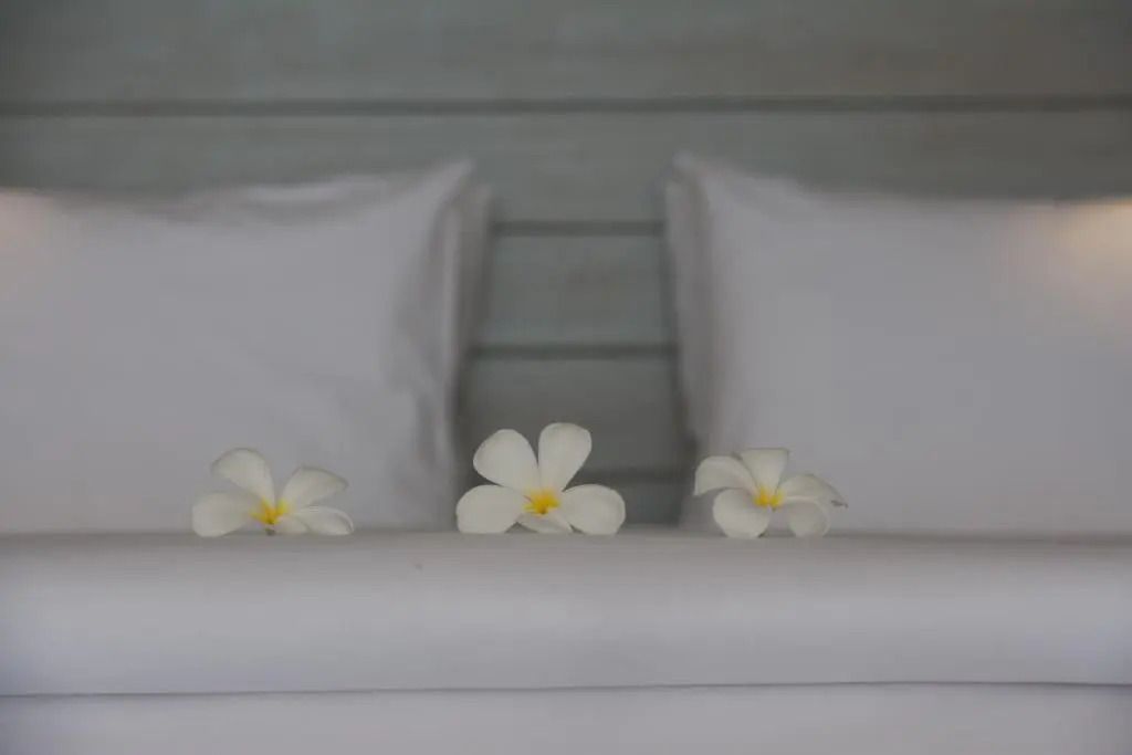 Detailaufnahme eines Betts mit weißen Kissen und Frangipani-Blüten
