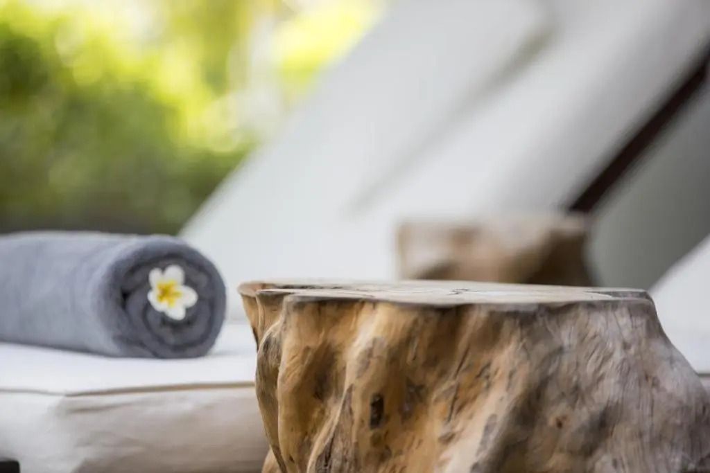 Nahaufnahme eines Holzbeistelltisches neben gerolltem Handtuch mit Blüte