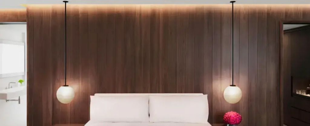 Holzverkleidete Wand mit dezentem Beleuchtungskonzept hinter einem eleganten Bett