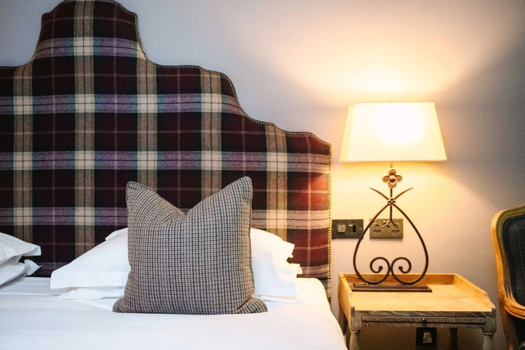 Detail eines Hotelbetts mit kariertem Kopfteil und stilvoller Nachttischlampe.