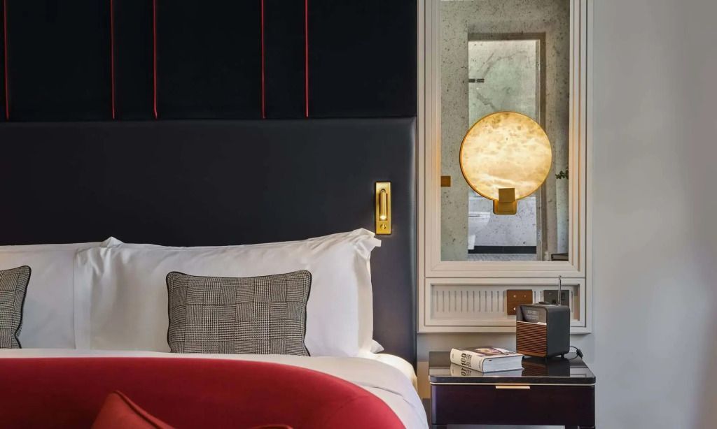 Teilansicht eines eleganten Hotelbetts mit roter Decke und Nachttisch mit Lampe