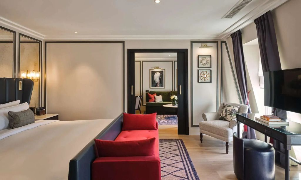 Elegante Suite mit Doppelbett, rotem Sofa und Sitzbereich im The Mayfair Townhouse