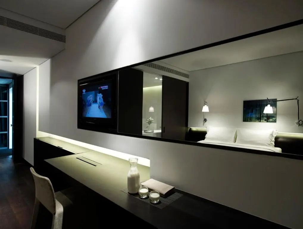 Zimmer mit Schreibtisch, großem Spiegel und Wand-TV, moderne Beleuchtung.