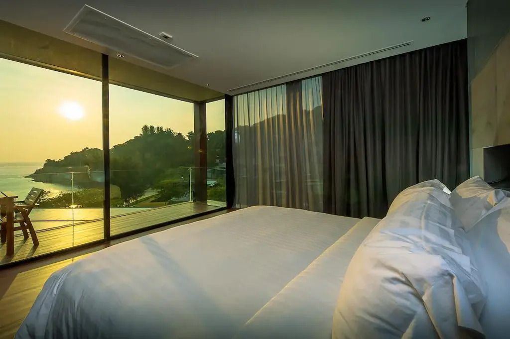 Schlafzimmer mit Bett und Panoramafenstern, Blick auf die Landschaft im Sonnenuntergang.