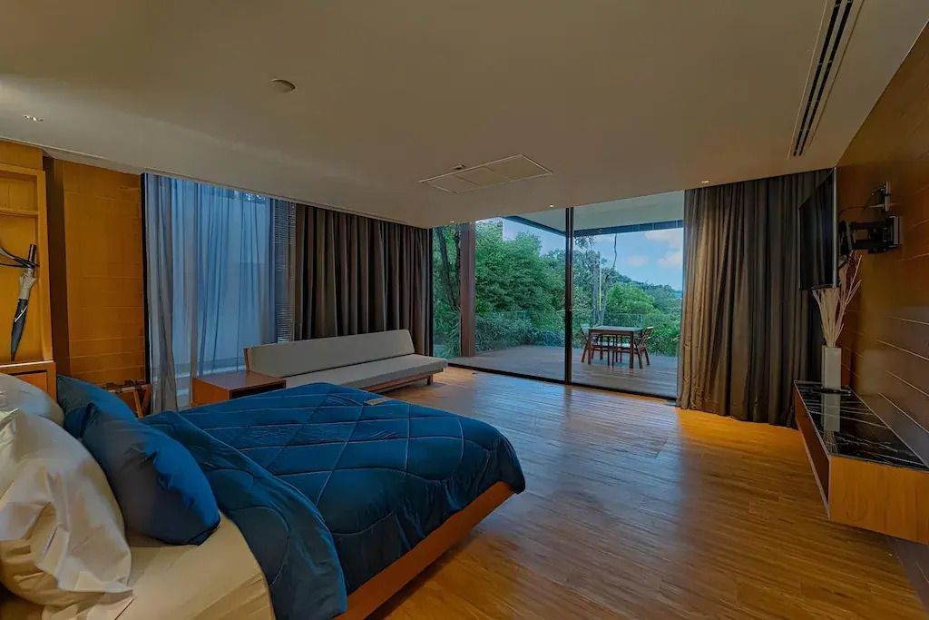 Großzügiges Schlafzimmer mit großem Fenster. Blick auf Terrasse und naturbelassene Umgebung.