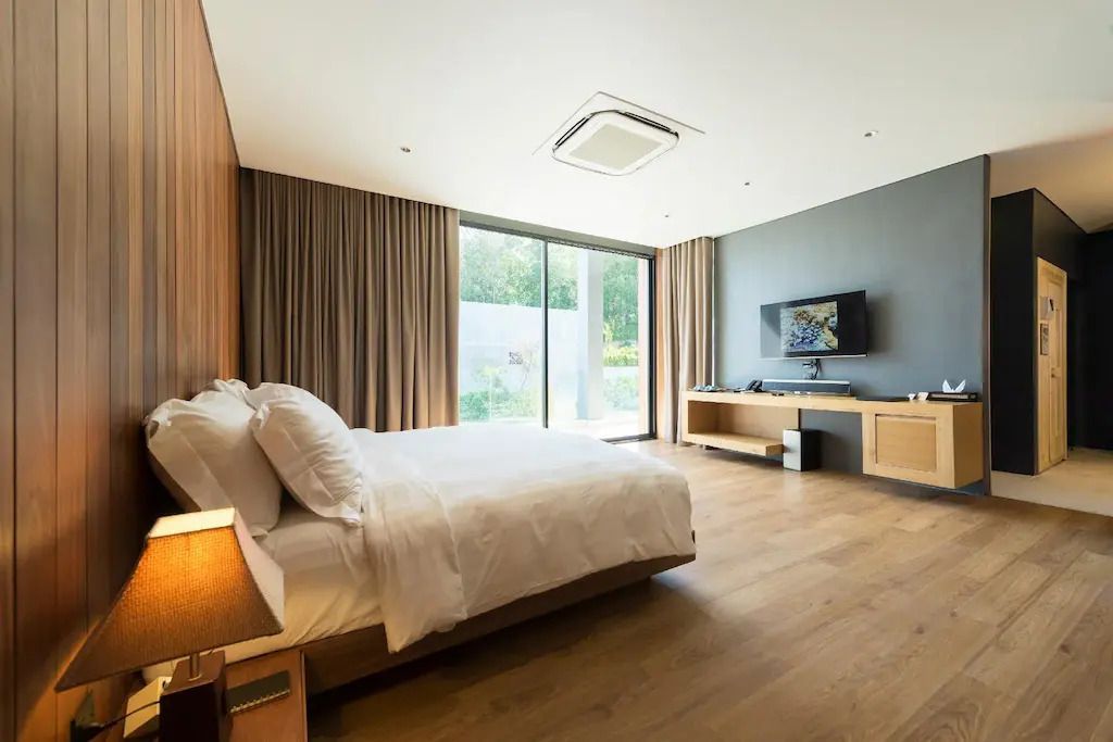 Modernes Hotelzimmer mit Doppelbett, Holzboden und großer Fensterfront mit Blick ins Grüne.