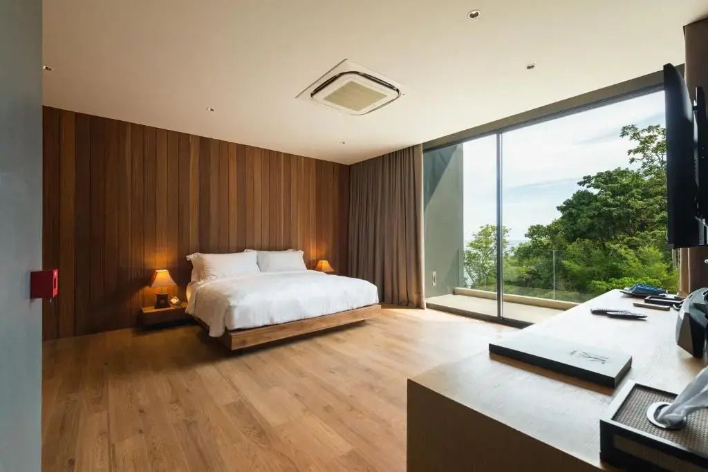 Helles Schlafzimmer mit Doppelbett, Holzwandverkleidung und Blick vom Balkon auf die Berge.