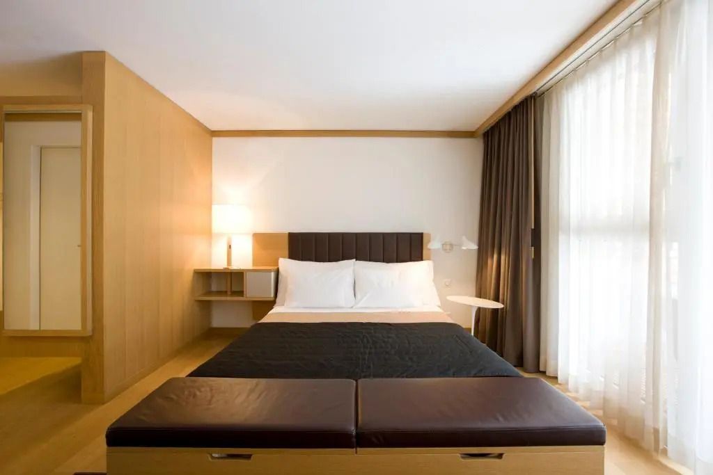 Doppelbett im Hotelzimmer mit großen Fenstern und Vorhängen