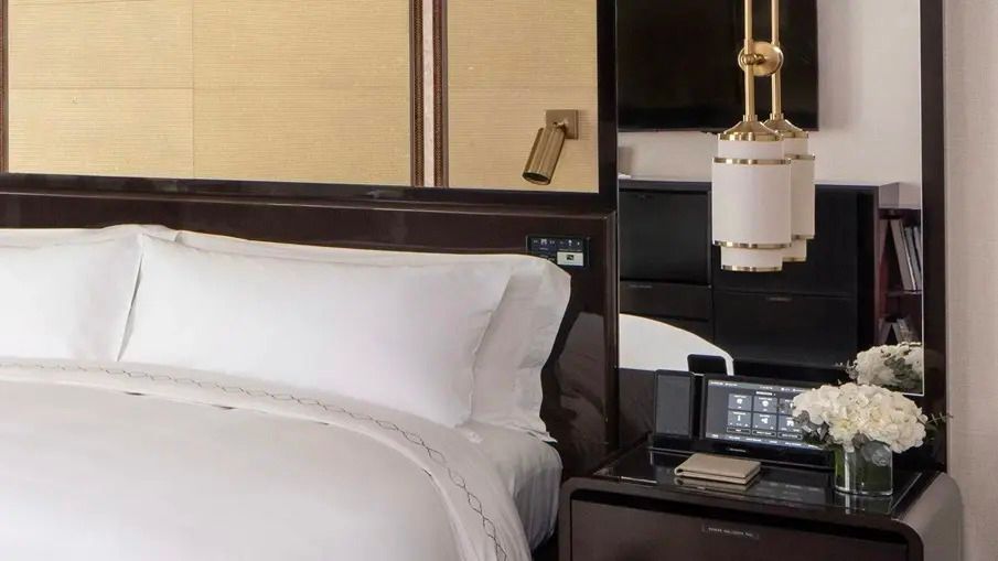 Nahaufnahme eines Nachttisches mit moderner Beleuchtung und Bett in einer Suite