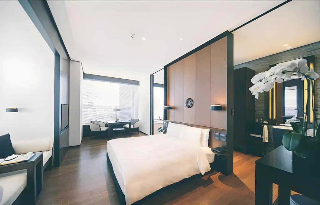 Geräumiges Deluxe Doppelzimmer mit elegantem Bett und Sitzbereich. Große Fensterfront.