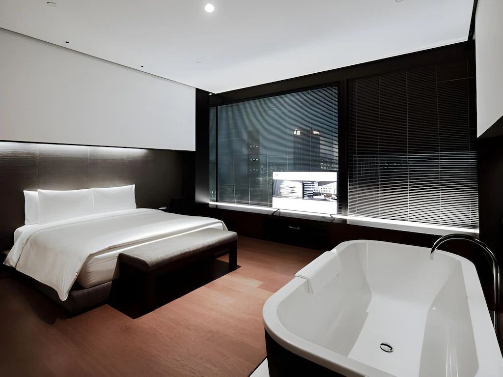 Luxuriöses Schlafzimmer der Jing'An Suite mit freistehender Badewanne und großer Fensterfront.