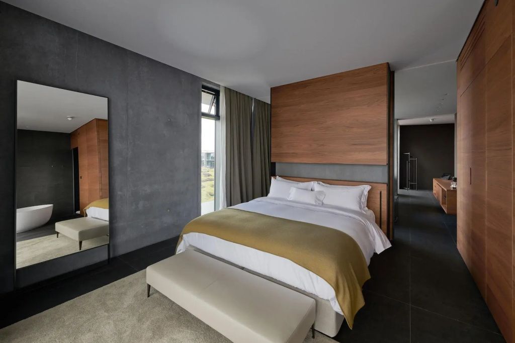 Luxuriöses Suite Schlafzimmer mit Kingsize Bett, Spiegel und warmen Holzelementen.