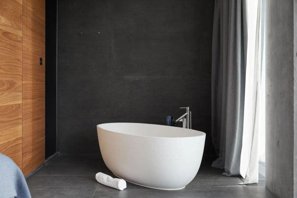 Freistehende weiße Badewanne im eleganten dunklen Badezimmer einer Suite.