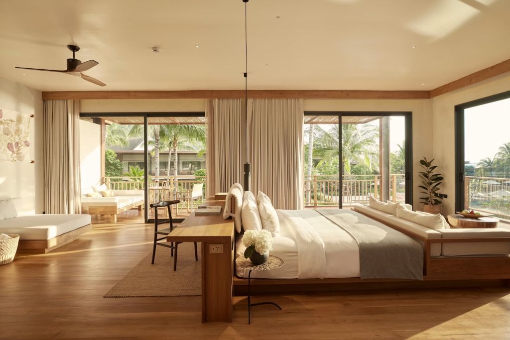 Elegante Suite mit modernem Doppelbett und weitläufigem Balkon mit Sitzbereich.