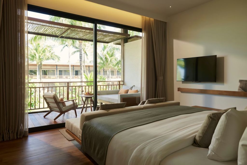 Helles Zimmer mit Doppelbett und Zugang zum Balkon mit Palmenblick