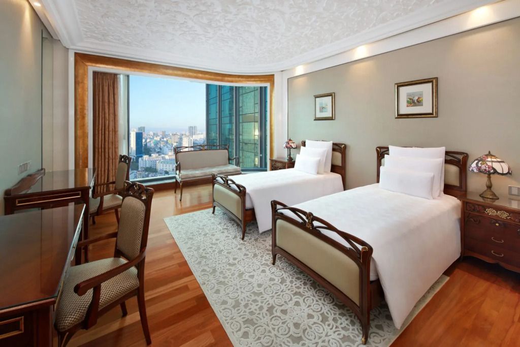 Zweibettzimmer mit großen Fenstern und Ausblick auf die Stadt.