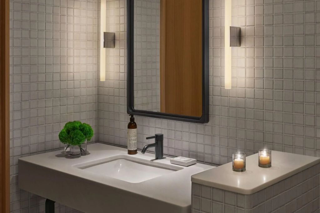 Modernes Badezimmer im Reykjavik Edition mit feinen Fliesen, stilvollem Waschtisch und sanftem Kerzenlicht.